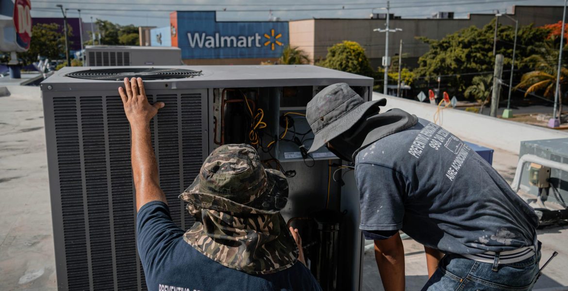 Two technicians repair a rooftop HVAC unit outside a Walmart store.
